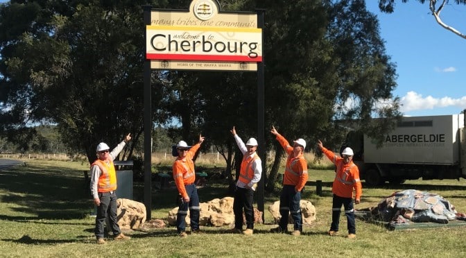 Construction workers pointing up at a Cherbourg sign